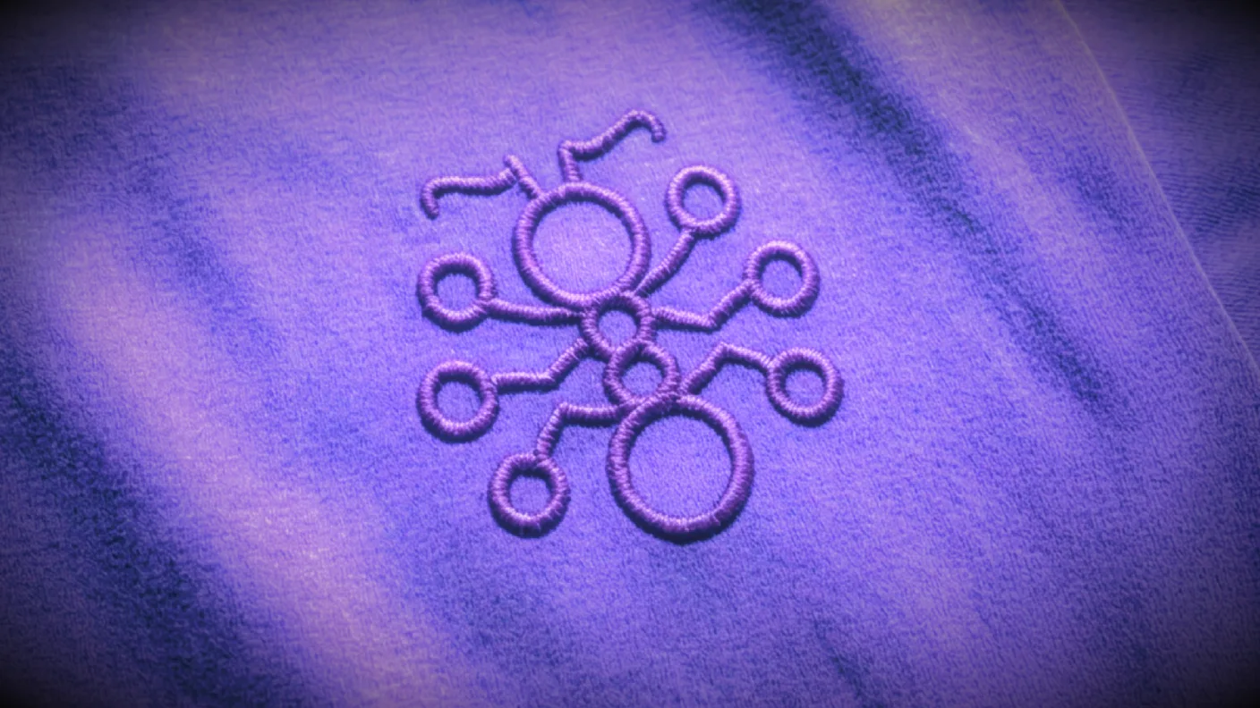 The DeFi Collective mark embroidered in violet thread on heather-purple fabric: linked rings and stems that read as both an ant and a network of connected nodes.